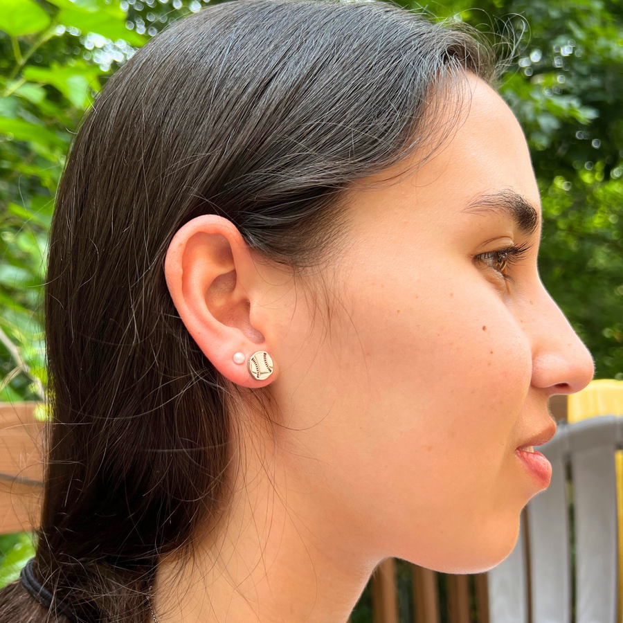 Lifestyle image of cute minimalist baseball stud earrings from the side. Lifestyle image of softball stud earrings from the side.